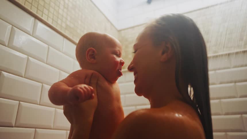 A loving mother holds her newborn baby and kisses them tenderly while they shower together