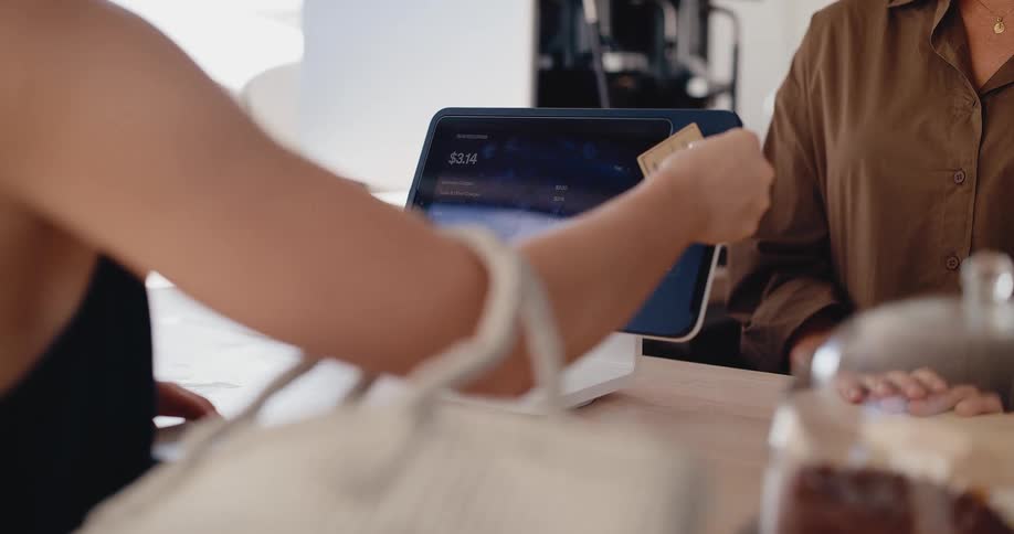 A customer uses a credit card to make a contactless payment at a cafe using a point-of-sale terminal