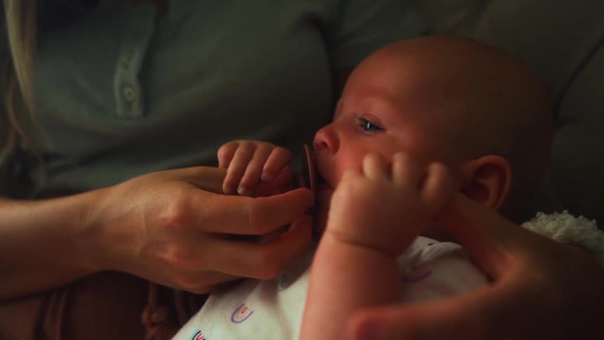 A loving mother gently holds her newborn baby's hands as the infant rests calmly with a pacifier