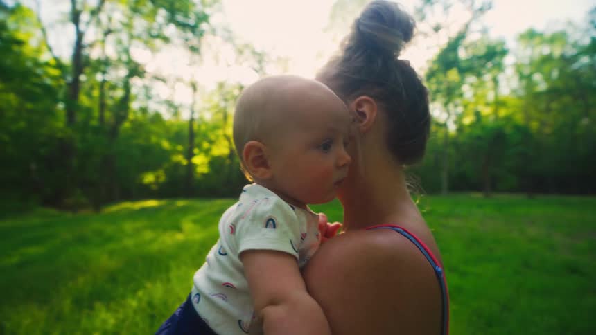 A tender moment between a mother and her baby as she holds him in a sun-dappled green field