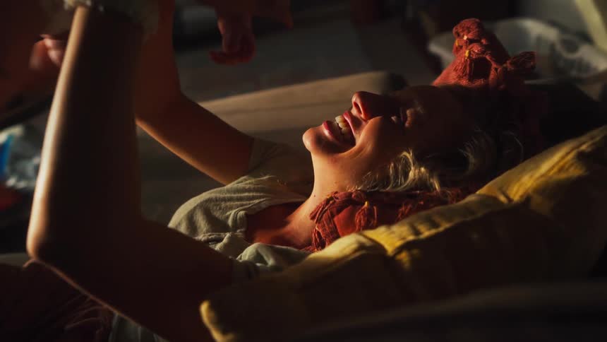 A joyful mother plays with her adorable baby on the couch in slow motion, basking in the warm afternoon sunlight