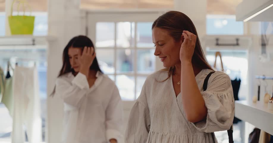 Two stylish women browse a bright and airy clothing boutique in slow motion