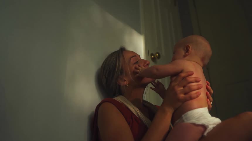 A mother and her baby share a tender moment in a dimly lit room as the baby touches her face