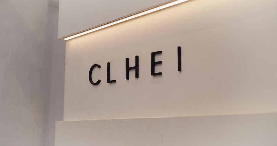 A minimalist black letter sign on an off-white wall is illuminated by a warm recessed light strip