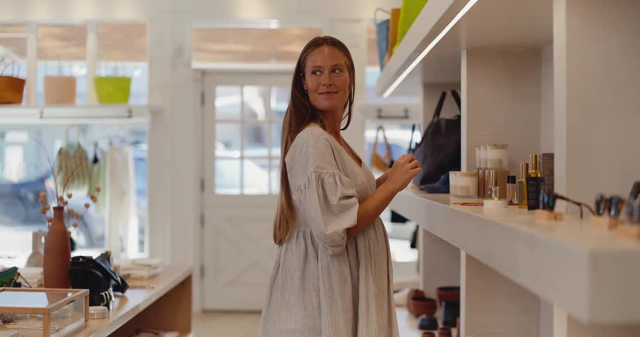 A beautiful pregnant woman in a stylish boutique smiles as she tests a perfume on her wrist
