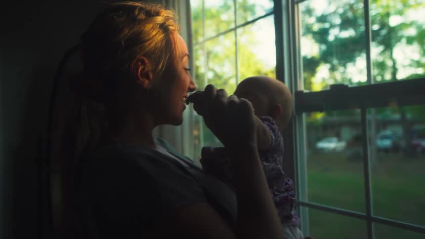 A tender moment between a mother and her newborn baby, silhouetted against a window at golden hour