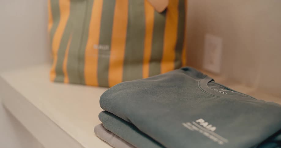 A close-up slow-motion push-in on neatly folded t-shirts and a striped tote bag displayed on a shelf in a modern boutique