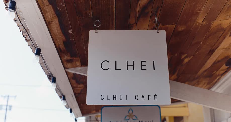 A modern white cafe sign hangs from a rustic wooden awning decorated with string lights