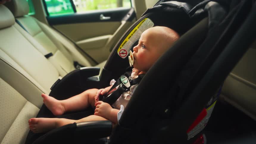 A content baby with a pacifier sits patiently in a rear-facing car seat in the back of a vehicle