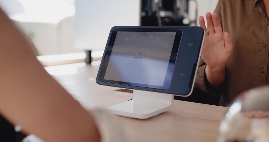 A customer adds a tip and completes a contactless payment on a tablet POS system at a cafe counter