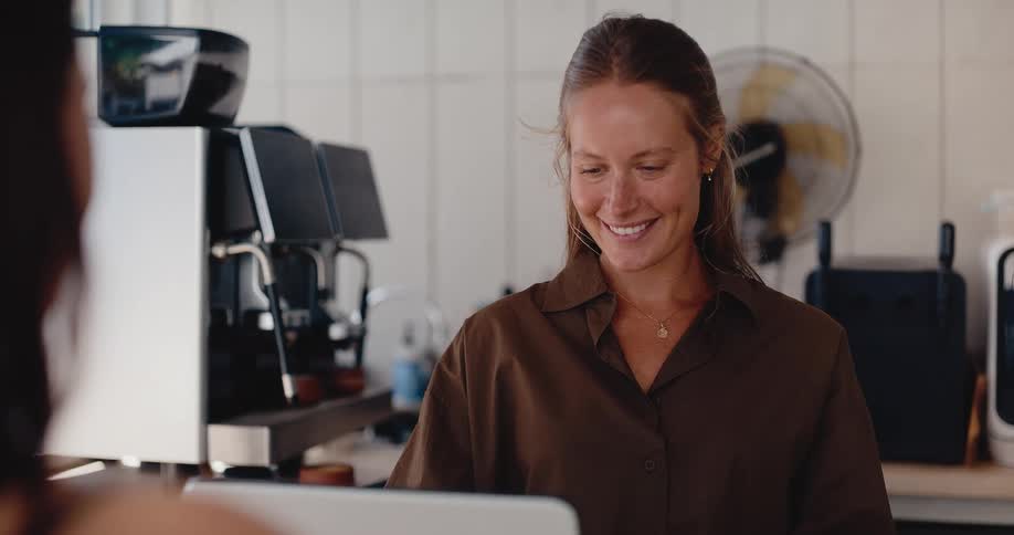 A friendly female barista smiles warmly while taking a customer's order at the counter of a modern coffee shop