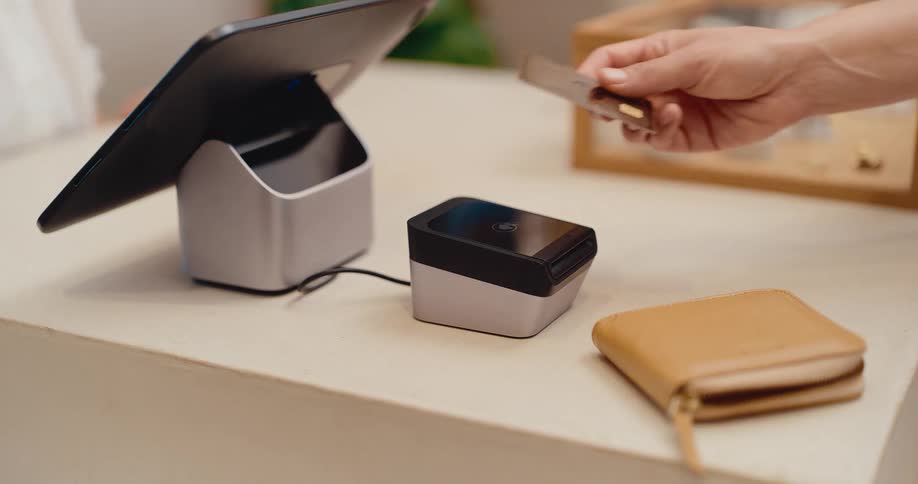 Close up slow motion of a customer making a contactless payment by tapping a credit card on a reader at a retail store counter