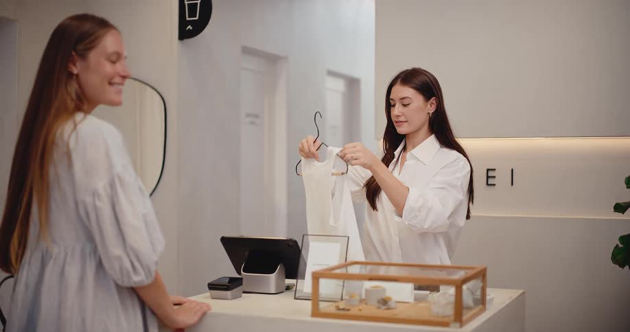 A cheerful shop assistant prepares a customer's purchase at the counter in a stylish, modern clothing store