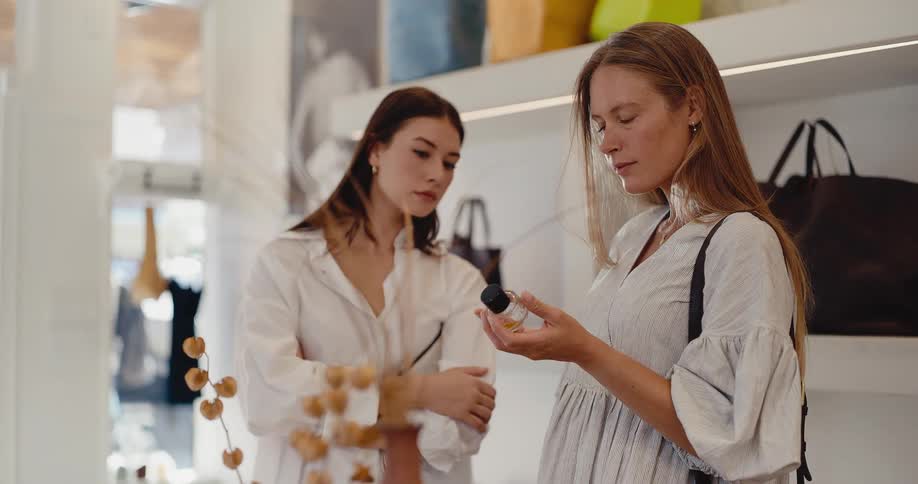 Two stylish women thoughtfully examine a perfume bottle while shopping in a bright, modern boutique