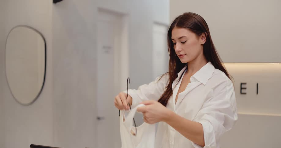 A friendly young female shop assistant takes a customer's items at the checkout counter and prepares them for purchase in a modern boutique