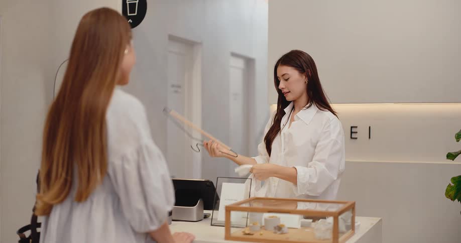 A friendly shop assistant in a minimalist boutique carefully folds a customer's purchased top at the checkout counter