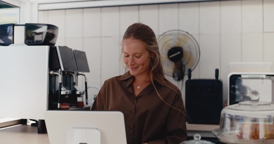 Portrait of a friendly and smiling female barista standing behind the counter of a modern coffee shop