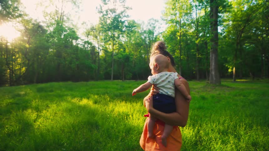 A loving mother gently holds her infant in a beautiful sun-drenched meadow at golden hour, introducing the baby to nature
