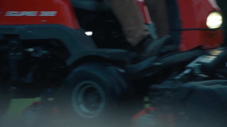 A close-up slow-motion shot of a red industrial lawn mower cutting a lush green lawn at dawn