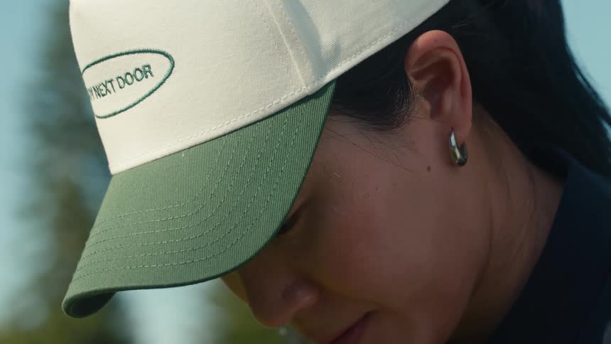 A close-up of a focused Asian woman wearing a baseball cap as she concentrates on her golf game