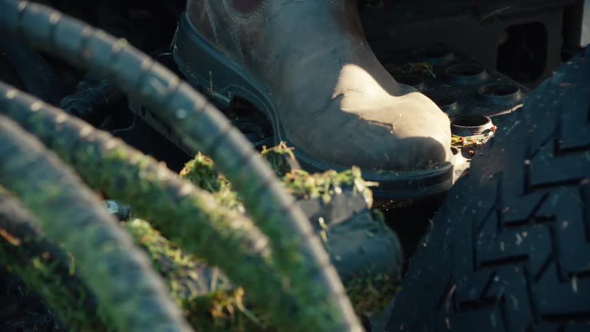 A close-up view of a farmer's dirty work boot stepping onto the metal running board of a farm vehicle
