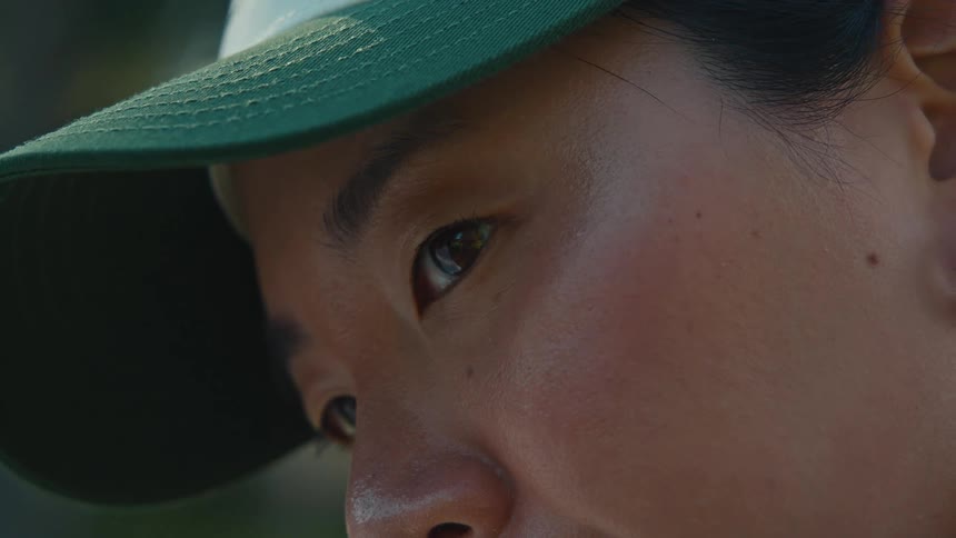An intimate close-up shot focuses on the ear, then the eye of a person wearing a baseball cap