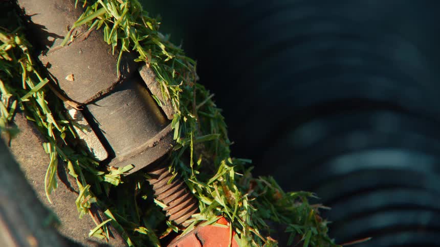 A detailed macro shot shows a metal bolt and component covered in fresh green grass clippings