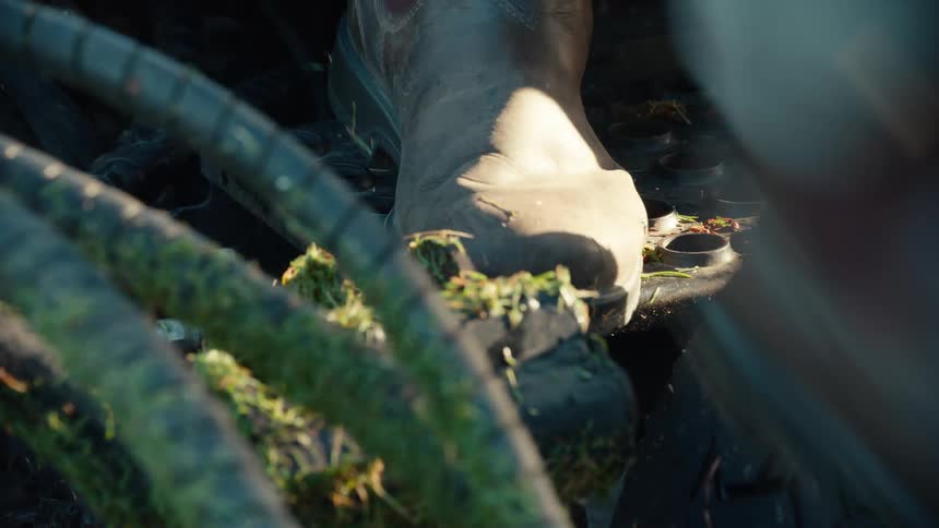 Close-up of a worker in a sturdy boot stepping onto the dirty, perforated metal step of a piece of heavy machinery