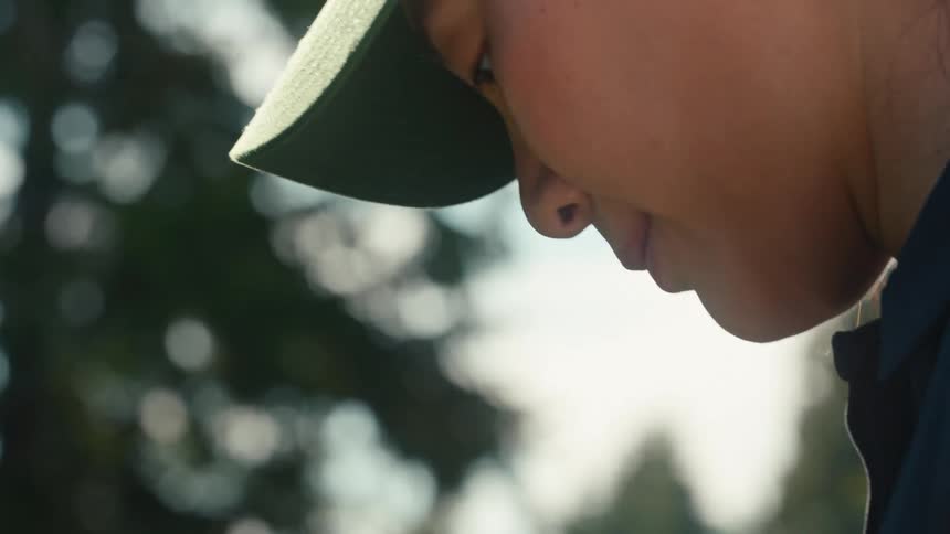A cinematic slow-motion close-up of a focused woman in a baseball cap looking up with a thoughtful expression