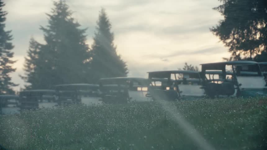 Sprinklers water a grassy hill with wildflowers as a row of golf carts sit parked in the misty background at sunrise
