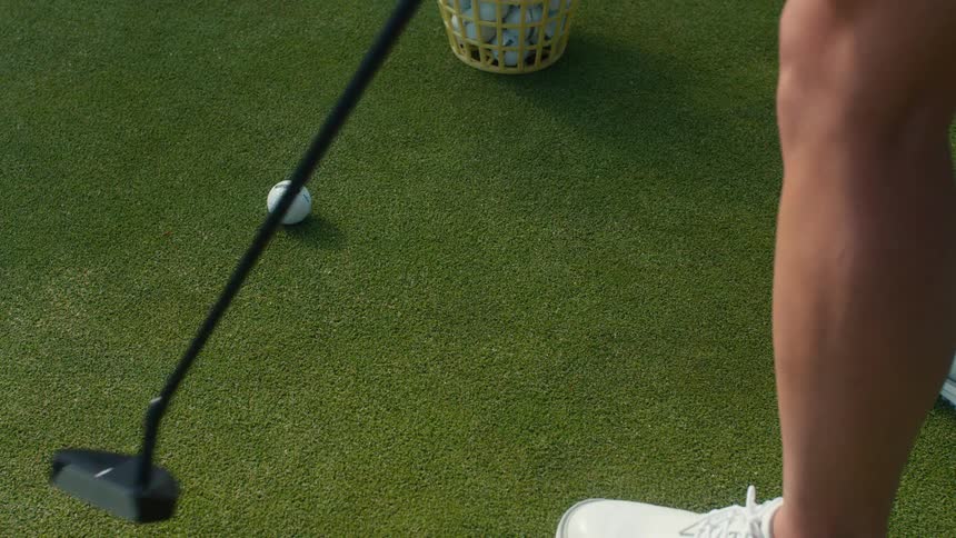 A high-angle slow-motion close-up of a golfer practicing their putt on a green, repeatedly hitting balls with a putter