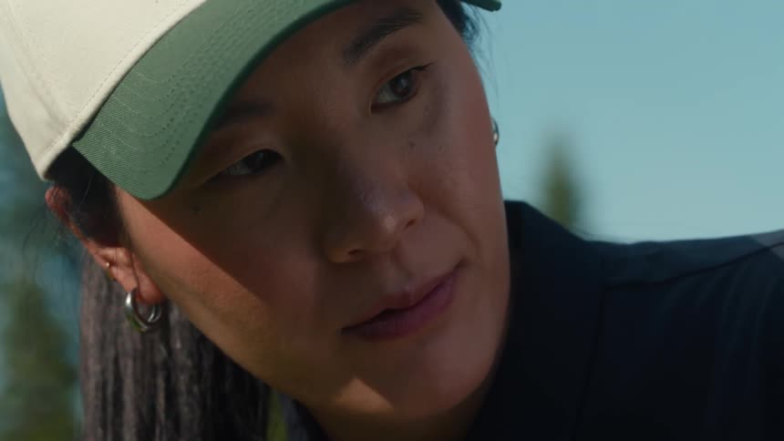 Extreme close-up shot on an Asian woman's face, showing her intense concentration as she plays golf on a sunny day