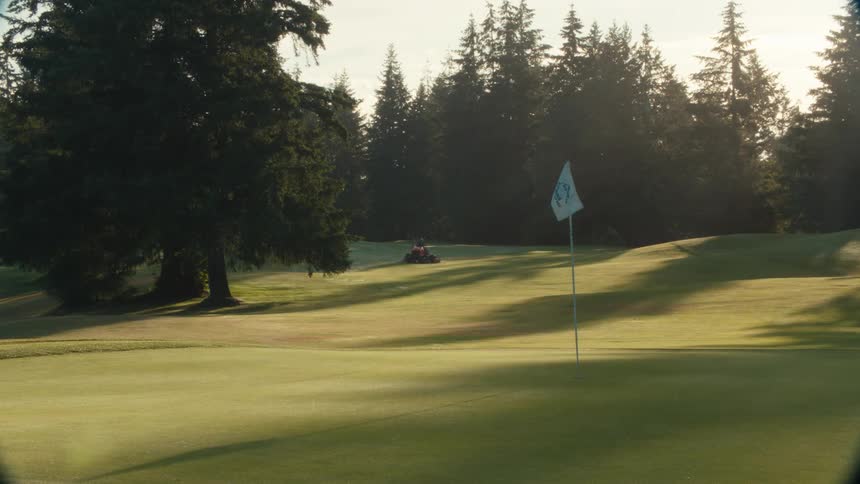 A groundskeeper mows the fairway on a serene golf course in the beautiful morning light