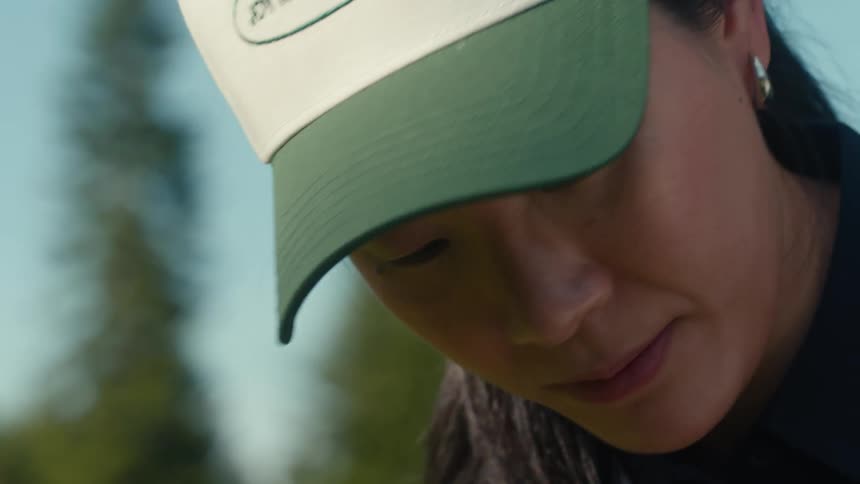 A close-up slow-motion shot of an Asian woman in a baseball cap concentrating intently on a sunny day outdoors