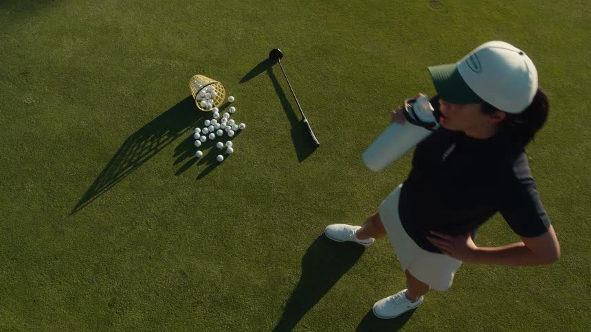 Top-down view of a female golfer taking a water break on a sunny putting green during practice
