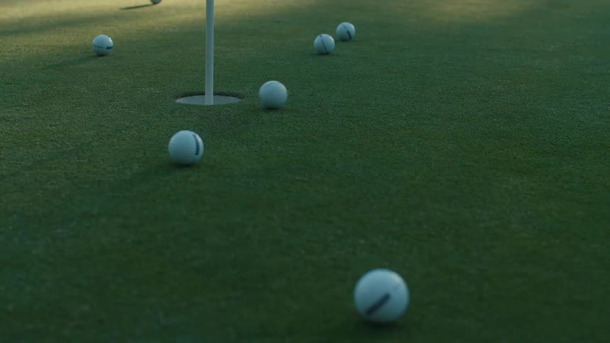 A golf ball is successfully putted into the hole on a putting green surrounded by other practice balls