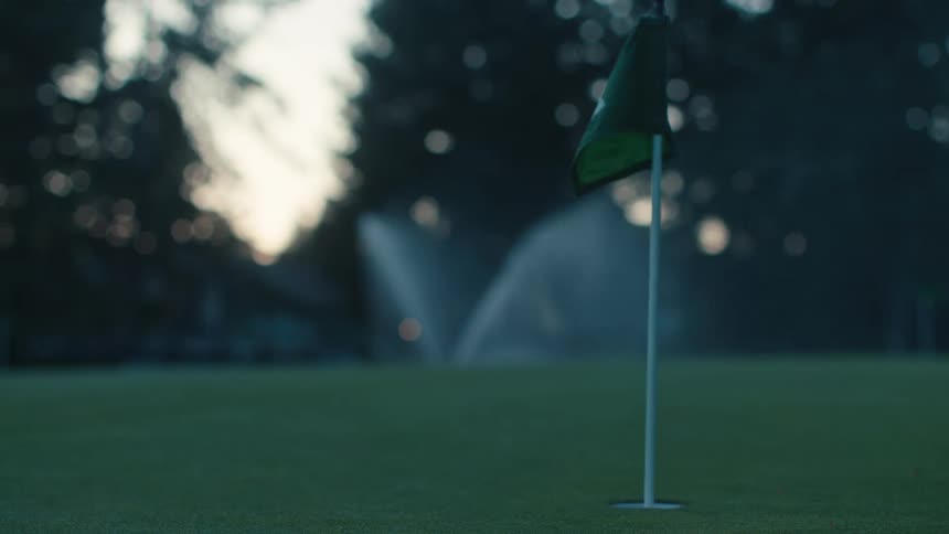 Sprinklers water an empty golf course green in the early morning light