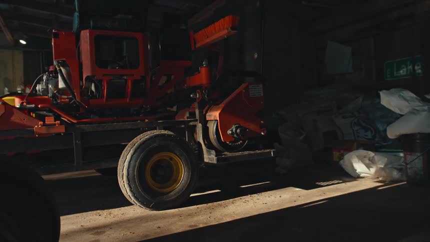 A red wood chipper sits inside a dark and dusty barn, illuminated by a single beam of sunlight