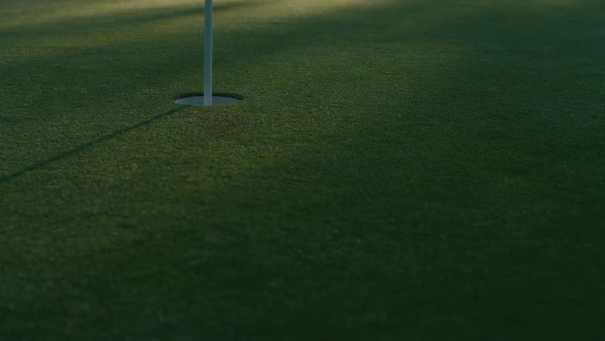 A golf ball rolls in slow motion across a perfectly manicured green and sinks into the hole for a successful putt
