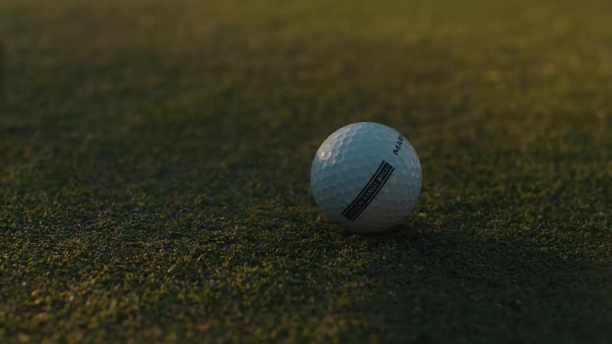 Close-up slow-motion of a putter striking a golf ball on a manicured green during golden hour