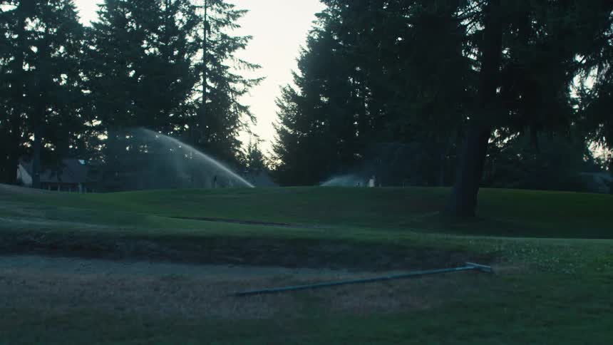 Automatic sprinklers water a lush, green golf course during the quiet hours of dusk