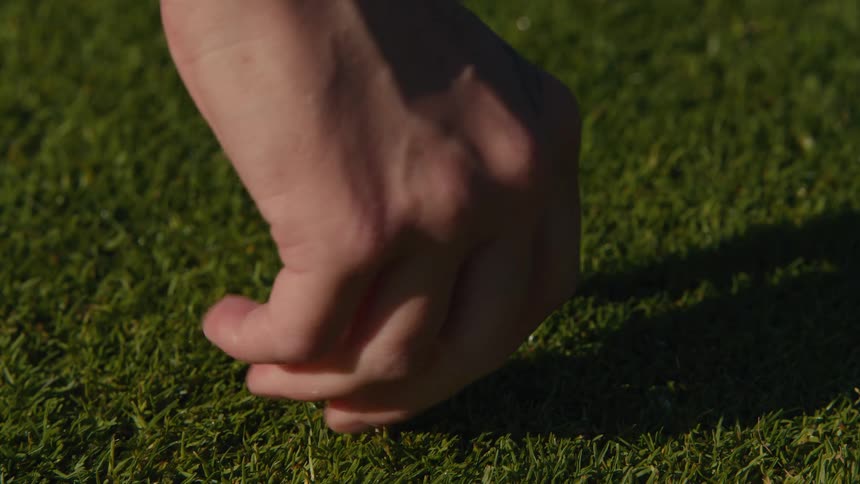 A hand pushes a tee into the lush green grass and places a golf ball on top in slow motion
