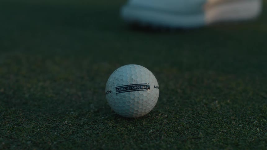 A slow-motion close-up of a putter striking a golf ball on a manicured green