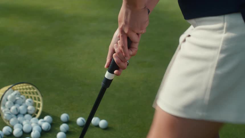 Close-up of a female golfer meticulously adjusting her hand grip on a club while practicing on a lush green