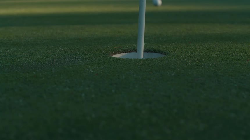 A golfer collects practice balls from a putting green next to the hole