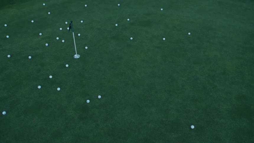 High angle shot of a golf ball rolling across a putting green scattered with practice balls
