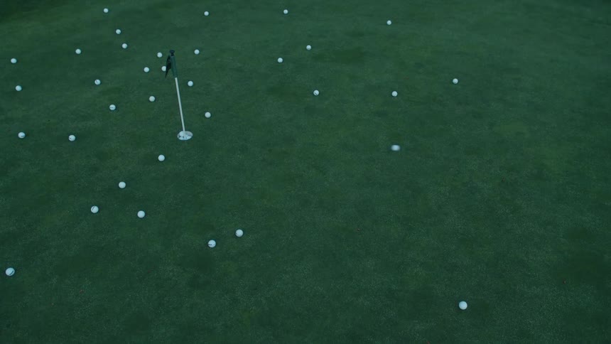 Overhead cinemagraph of a single golf ball rolling across a putting green scattered with many other balls