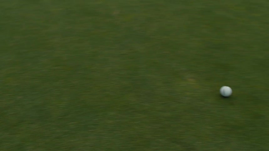 A golf ball rolls across a manicured putting green in a tracking close-up shot