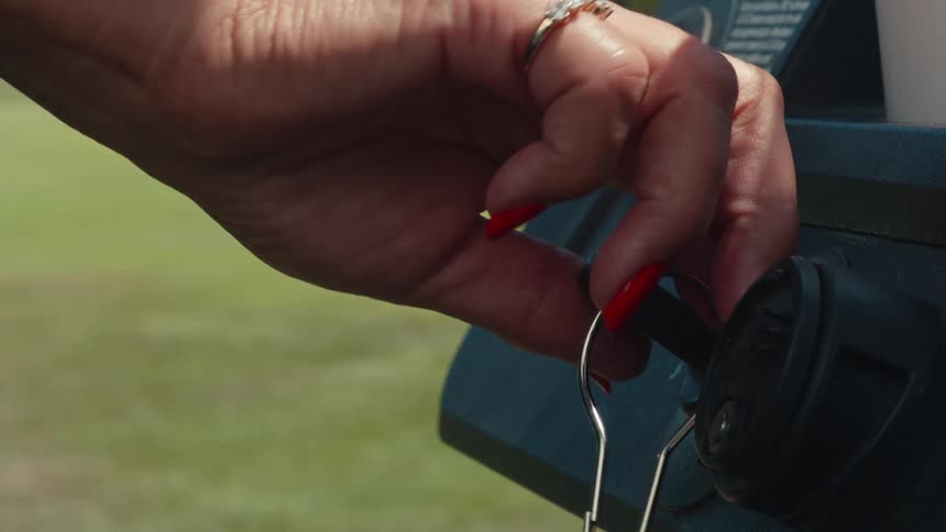 Close-up of a woman's hand with red nails putting a key in the ignition and starting a golf cart
