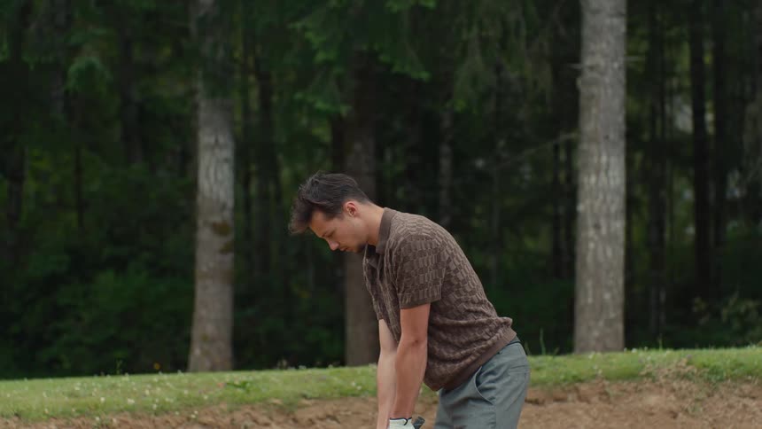 A skilled male golfer executes a powerful swing in slow motion, sending the ball and a cloud of sand flying out of a bunker